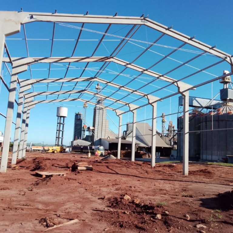 Estrutura de galpão industrial pré-fabricado em concreto com montagem de cobertura metálica em andamento, mostrando pilares, vigas e andaimes de apoio.